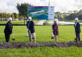 Four people in hardhats with shovels at the site of the new Palmer Florida building.