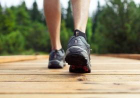 A man in sneakers walking away from the camera toward forested area.