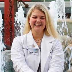 Woman in white clinic coat smiling in front of fountain.