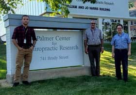 Three men in front of Palmer Center for Chiropractic Research sign.