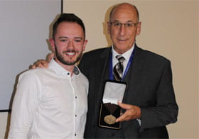 Two men smiling, holding a medal award.