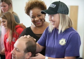 Dr. Teri Payton smiling while a female student palpates a male student's neck.