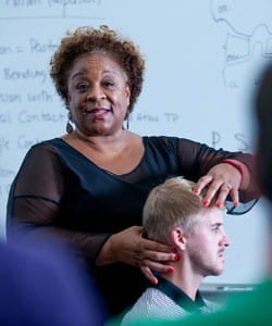 Woman in front of whiteboard adjusting a man's neck.