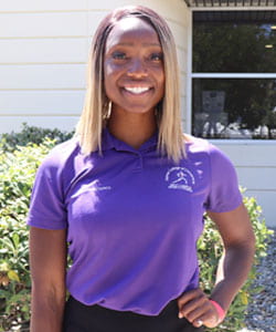 Alecia Beckford Steward smiling in a purple chiropractic polo.