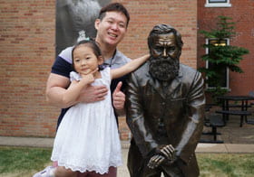 Kilbo Yun, Palmer Main student, and his daughter posing with the D.D. Palmer statue.