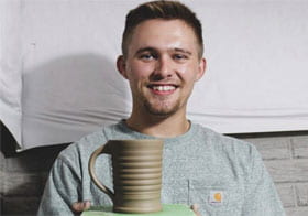 Tanner Zimmerman smiling and holding up pottery mug.