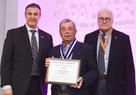 Three men in suits holding a Fellows certificate