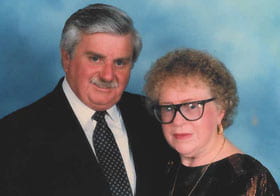 A couple in formal wear in front of blue background.