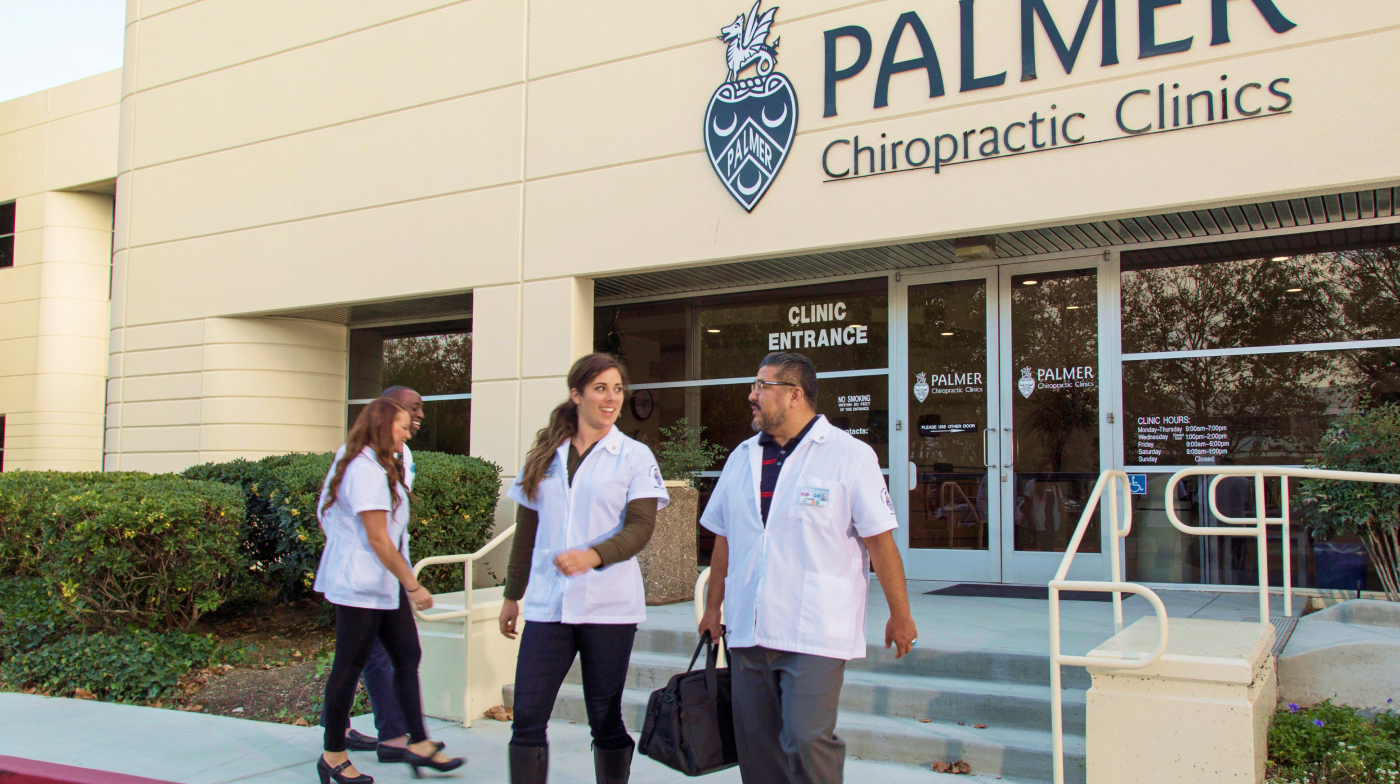 Student chiropractors in white clinic coats talking outside the Clinic.