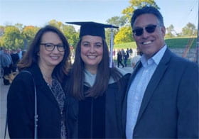 Faith Swartzendruber in graduation robe and hat with two adults.