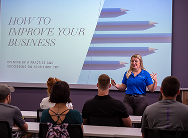 Woman instructing "How to Promote Your Business" to class of students.