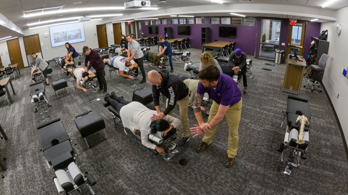 chiropractic students learning adjusting techniques from professors.
