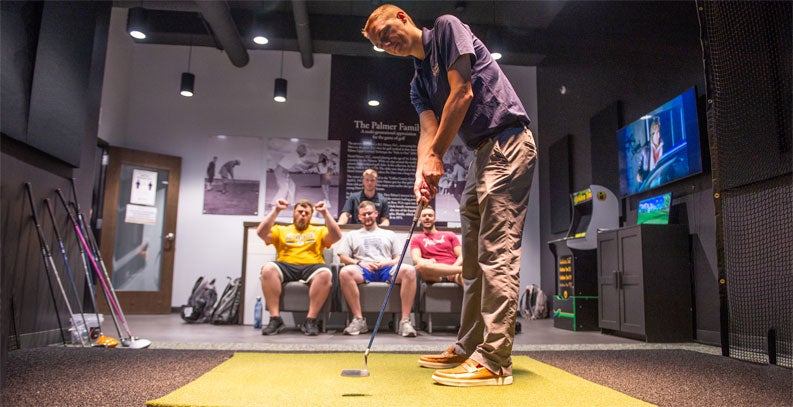 students cheering on a student using the golf simulator