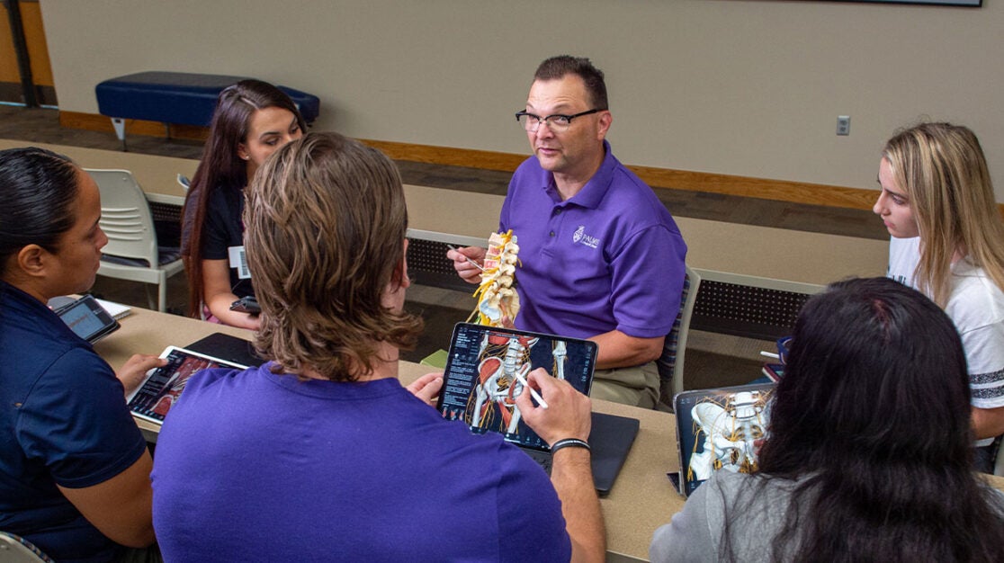 Group of students using 3D for Medical program on iPads and observing instructor pointing at spine model.