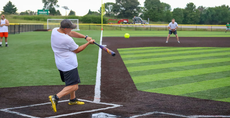 man hitting softball on baseball field