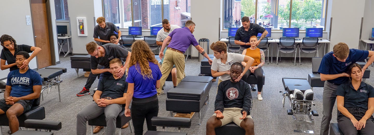 Students learning a chiropractic adjustment with help of faculty members.