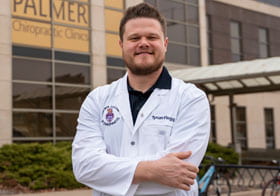 Tynan Flegg, Palmer Main student, in white coat in front of Palmer Clinic building.