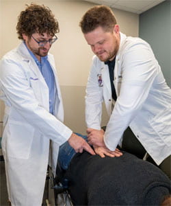 Dr. Percuoco and student Tynan Flegg adjusting client's lower back.
