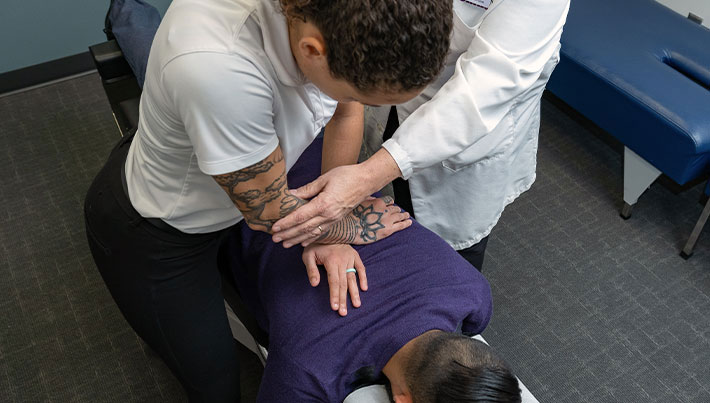 Instructor and student in white clinic coats adjusting client's back