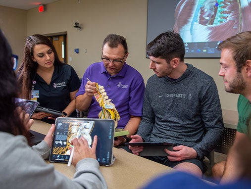 Students reviewing skeletal model on iPad as instructor points to real-life skeletal model.