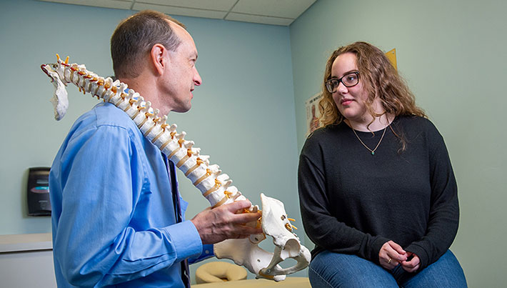 Chiropractic researcher talking to a patient, holding a spine model.