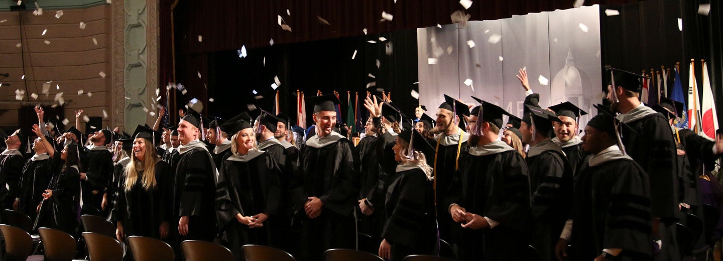 group of students in graduation gowns throwing cards into the air