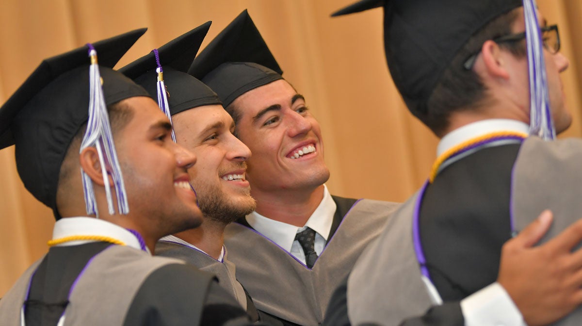 Four students in graduation caps and gowns taking selfie.