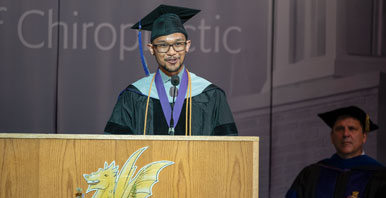 student in graduation gown speaking at podium