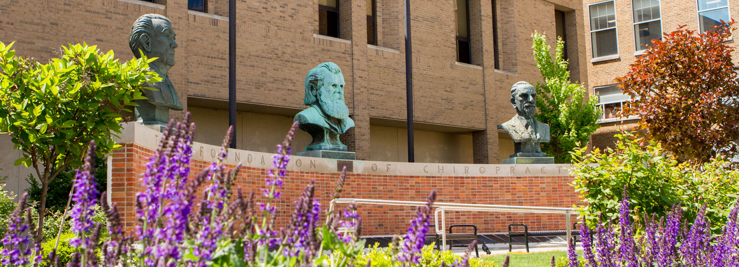 Brick wall with three busts behind purple flowers
