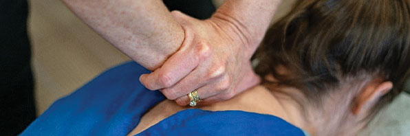 Close up of hands adjusting a woman's neck and shoulder.