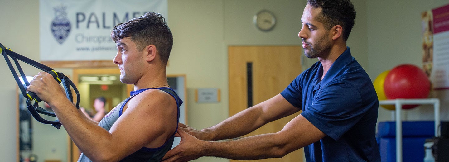 student adjusting athlete's movement while using exercise machine