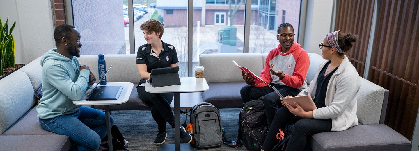 Four students studying together, sitting on couches in front of a window at Palmer College