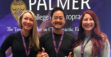 Three Palmer alumni standing in front of a banner