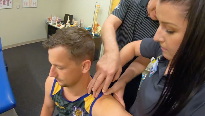 Faculty clinician and student palpating patient's shoulder.