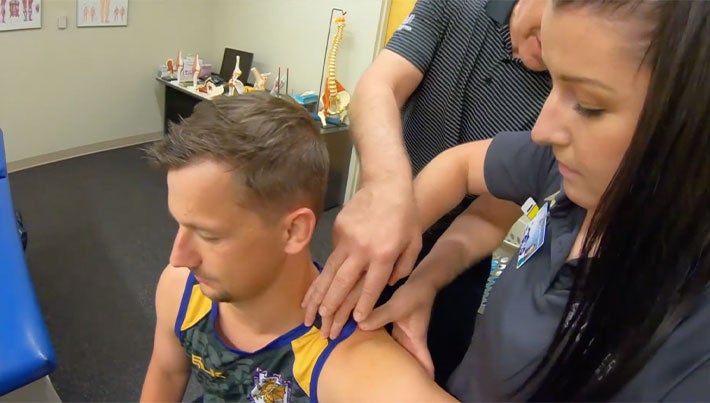 Faculty clinician and student palpating patient's shoulder.