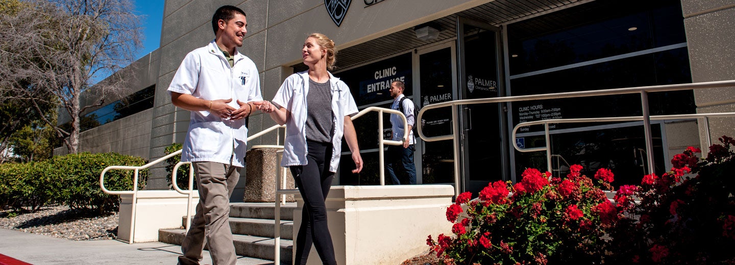 Clinic students in white coats talking in front of West Campus clinic entrance.