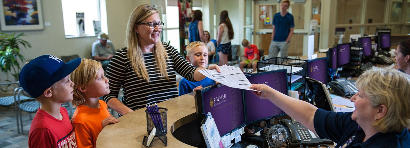 A mom and her children checking in for a chiropractic appointment at Palmer Chiropractic Clinics.