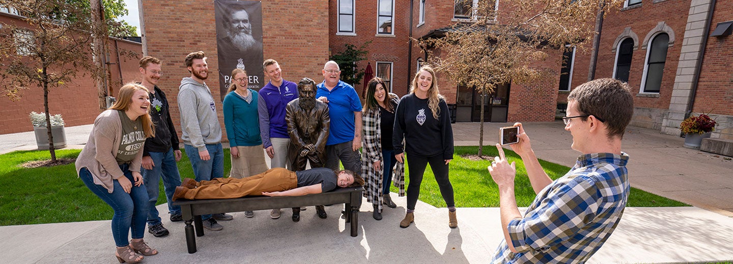 group of students having photo taken near D.D. Palmer First Adjustment statue.