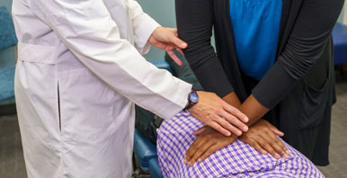 Clinic instructor's hands correcting student's hands on patient's back