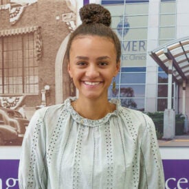 Intern of the Month Kaylee Harris smiling in front of Clinic wall.