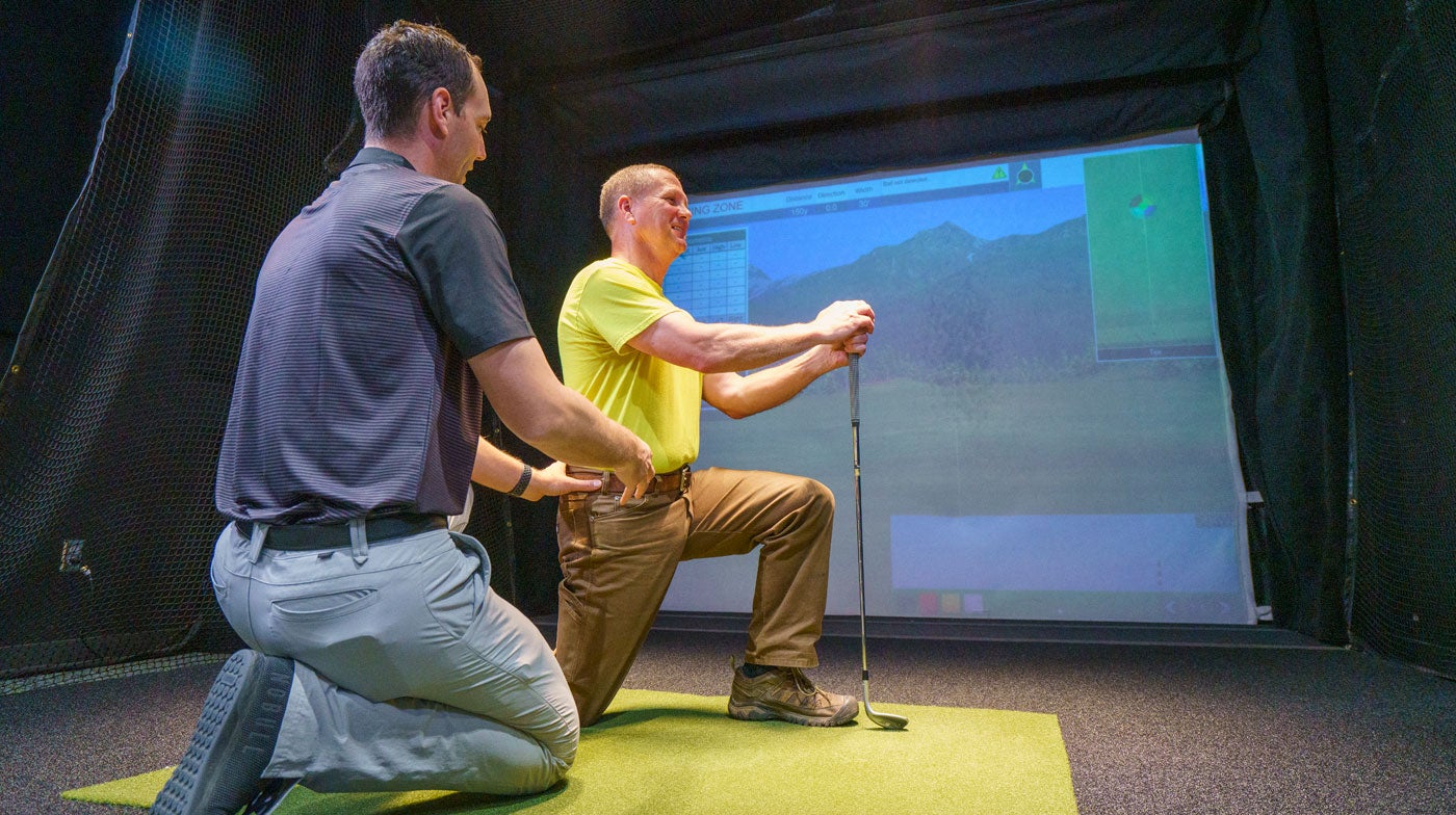 Dr. Buns helping golfer stretch at golf simulator.