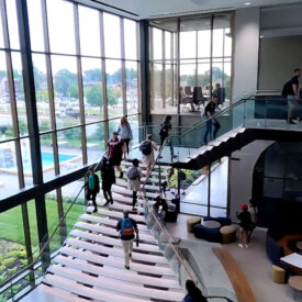 students walking down large staircase surrounded by windows