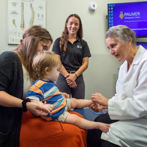 Dr. Marriott examining baby sitting on mother's lap.