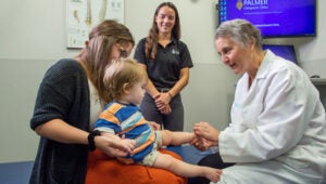 Dr. Marriott examining baby sitting on mother's lap.