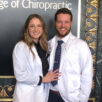 Couple in white clinic coats in front of Palmer College of Chiropractic in gold.