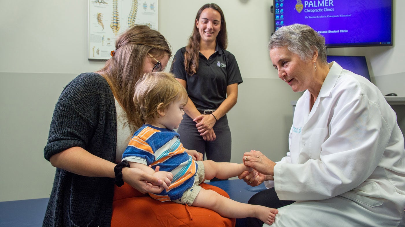 Dr. Marriott examining baby sitting on mother's lap.