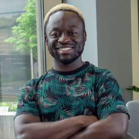 Michael Agyei smiling in Library with arms crossed.