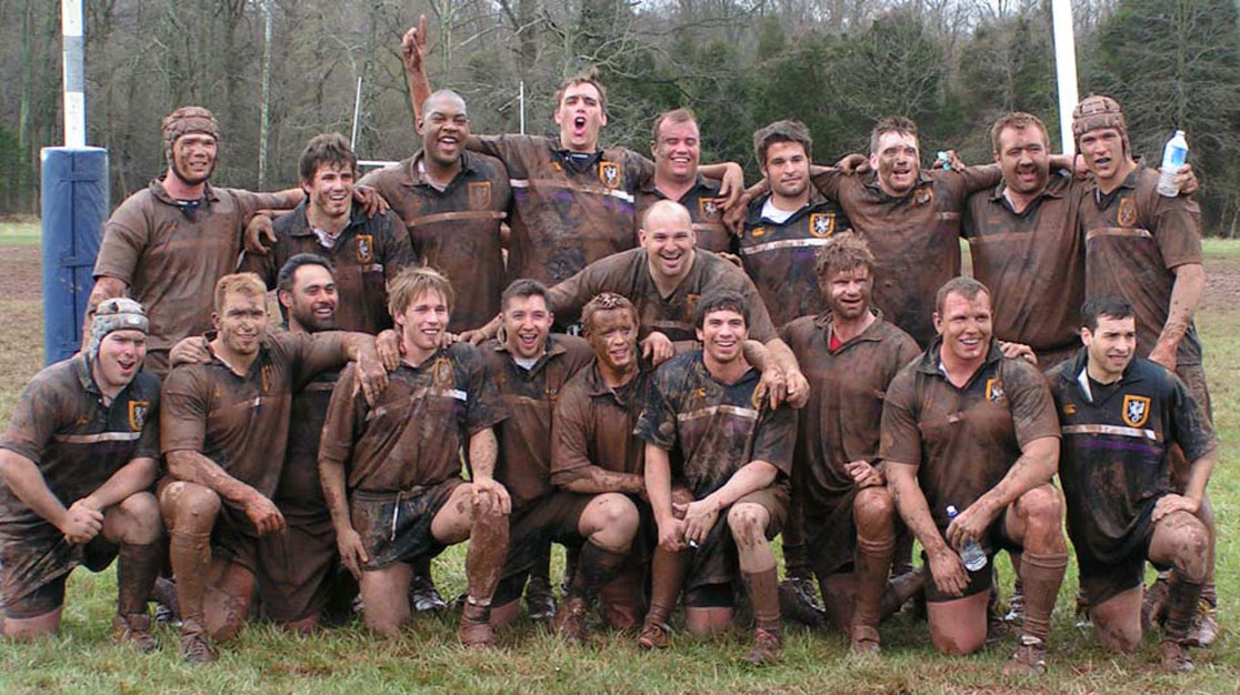 Group of men's rugby players outside covered in mud.