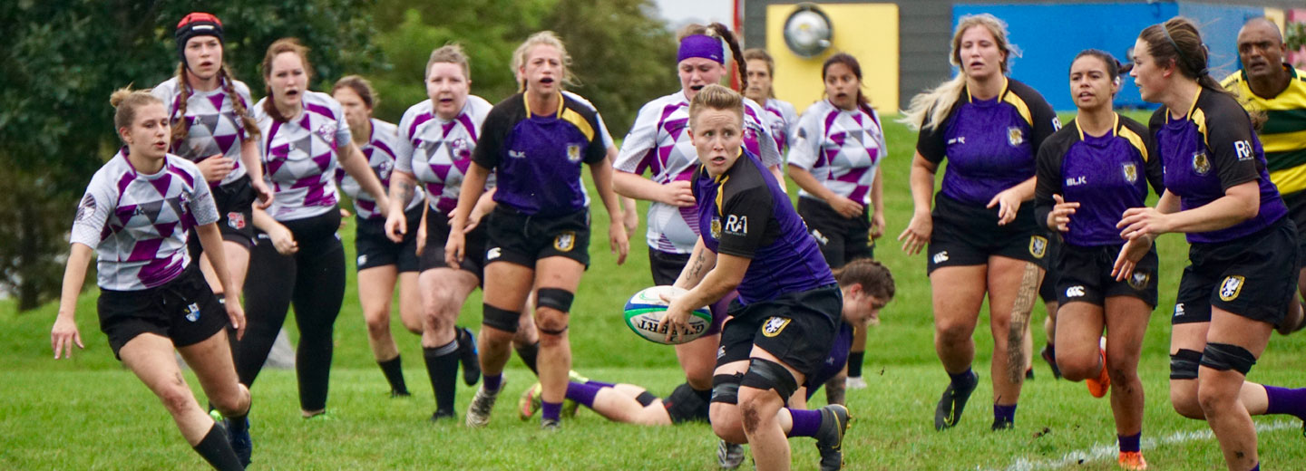 Two teams of women's rugby players running on pitch.
