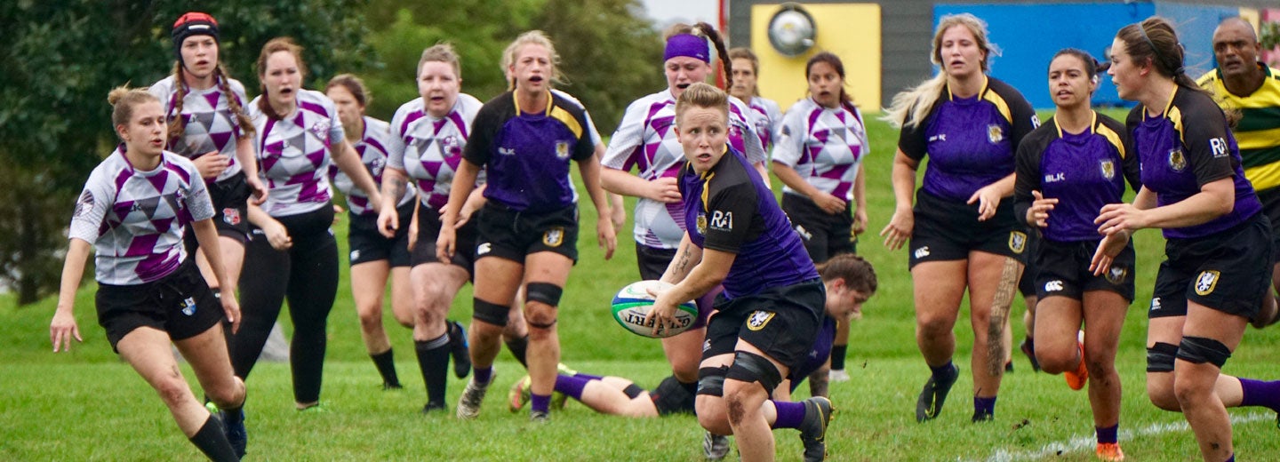 Two teams of women's rugby players running on pitch.